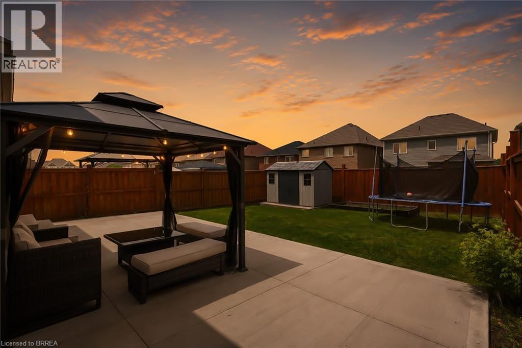 Expansive backyard featuring a concrete patio, a metal gazebo with string lighting, a wooden privacy fence, and a storage shed - 26 Pollard Street, Brantford, ON - Outdoor