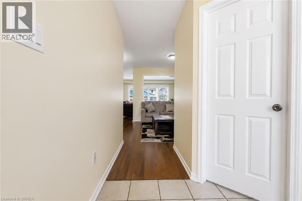 Hallway featuring light beige wall paint, wood-finish flooring, and a white paneled door with a dark knob - 26 Pollard Street, Brantford, ON - Indoor Photo Showing Other Room