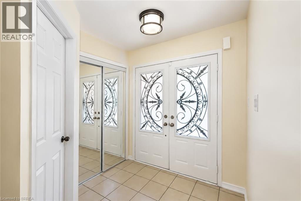 Double entry doors with intricate ironwork glass panels, tiled flooring, an overhead flush-mount light fixture, and mirrored closet doors - 26 Pollard Street, Brantford, ON - Indoor Photo Showing Other Room
