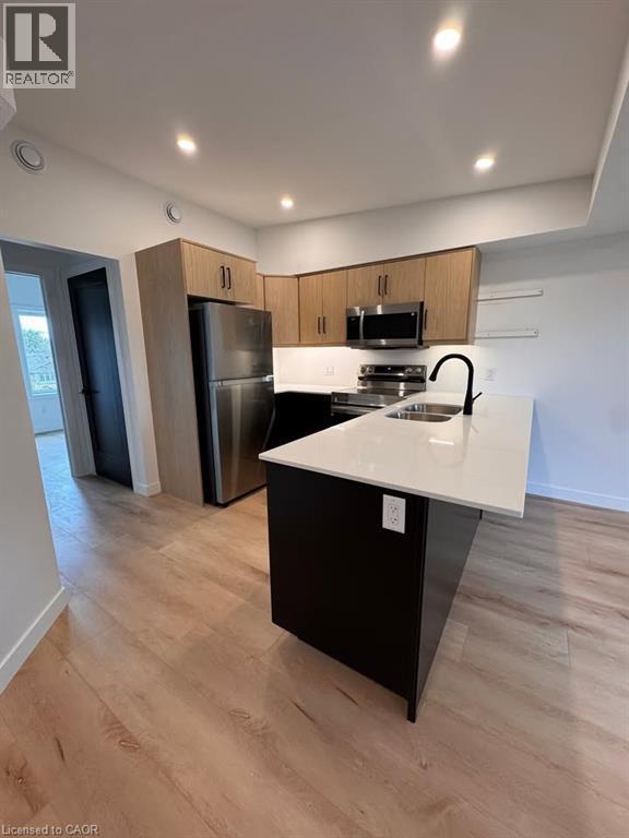 Modern kitchen featuring stainless steel appliances, light wood-finish cabinetry, a black kitchen island with a white countertop, a matte black faucet, and wood-finish flooring - 431 Krug Street, Kitchener, ON - Indoor Photo Showing Kitchen With Double Sink