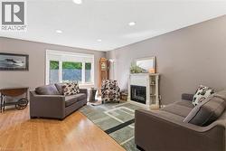 Living area featuring wood-finish flooring, recessed lighting, a large window, and a white decorative fireplace surround with an electric insert -