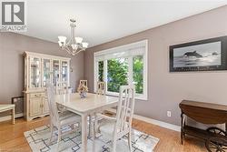 Bright dining area featuring wood-finish flooring, a contemporary five-light chandelier, and a large window with white trim -