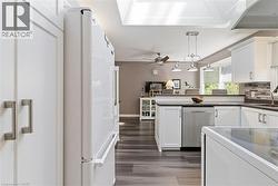 Kitchen featuring white cabinetry, stainless steel dishwasher, dark countertops, and a tiled backsplash -