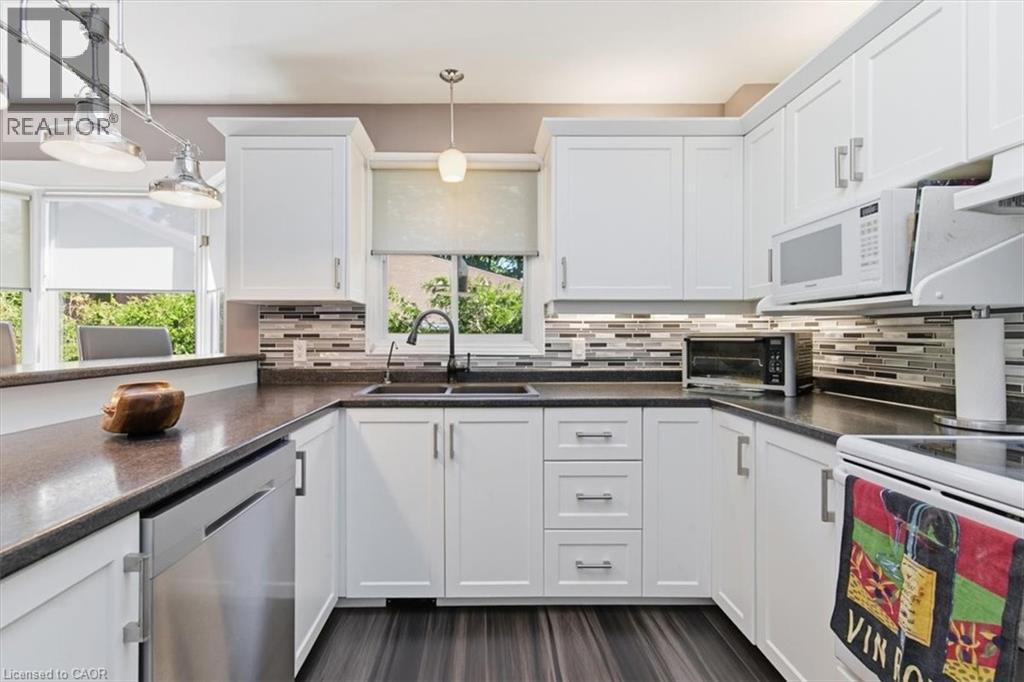 Contemporary kitchen featuring white cabinetry with brushed nickel hardware, dark wood-finish flooring, a mosaic tile backsplash, dark countertops, and a double basin sink with a gooseneck faucet - 26 Sideroad 18, Fergus, ON - Indoor Photo Showing Kitchen With Double Sink