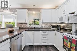 Contemporary kitchen featuring white cabinetry with brushed nickel hardware, dark wood-finish flooring, a mosaic tile backsplash, dark countertops, and a double basin sink with a gooseneck faucet -
