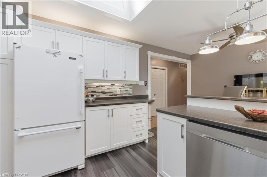 Kitchen featuring white cabinetry, dark countertops, a mosaic tile backsplash, wood-finish flooring, and a stainless steel dishwasher - 26 Sideroad 18, Fergus, ON - Indoor Photo Showing Kitchen