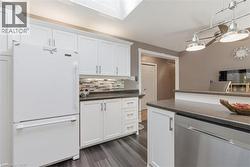 Kitchen featuring white cabinetry, dark countertops, a mosaic tile backsplash, wood-finish flooring, and a stainless steel dishwasher -