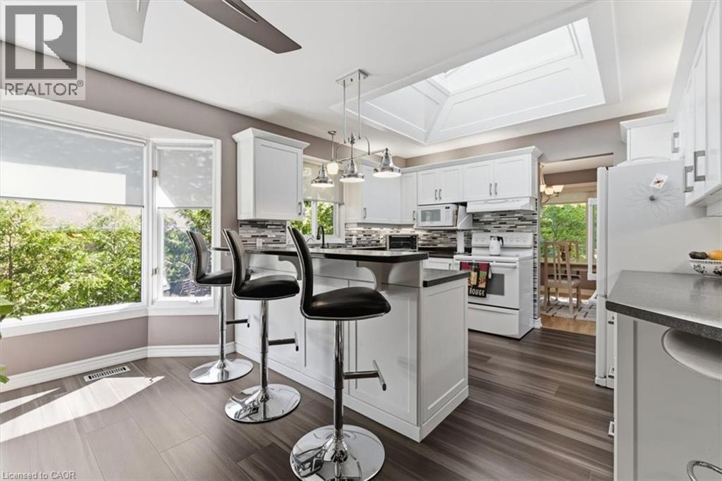 Kitchen featuring white cabinetry, dark countertops, a central island with pendant lighting, a skylight, and wood-finish flooring - 26 Sideroad 18, Fergus, ON - Indoor Photo Showing Kitchen