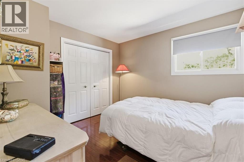 Interior room featuring wood-finish flooring, a double-door closet with white paneled doors, and an exterior window with a roller shade - 26 Sideroad 18, Fergus, ON - Indoor Photo Showing Bedroom