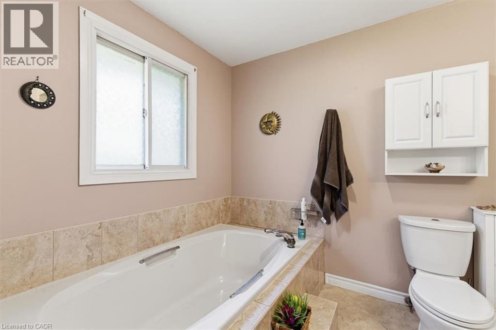 Soaking tub with a tiled surround, white sliding window, white wall-mounted storage cabinet with shelving, and tile flooring - 26 Sideroad 18, Fergus, ON - Indoor Photo Showing Bathroom