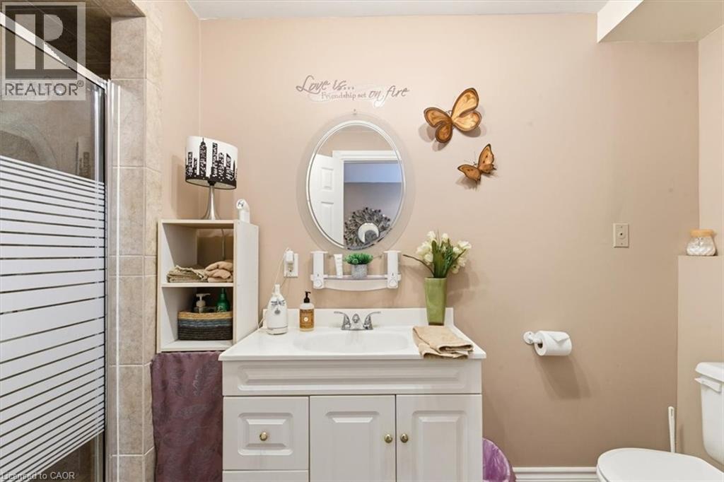 Bathroom featuring a white vanity with a single sink, an oval mirror, a shower with a frosted glass door, a toilet, and light-toned wall tile - 26 Sideroad 18, Fergus, ON - Indoor Photo Showing Bathroom