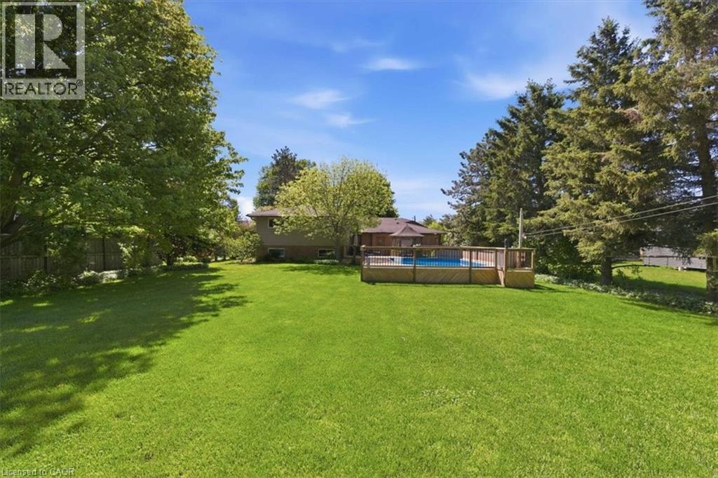 Expansive green lawn with a large, above-ground swimming pool featuring a surrounding wooden deck - 26 Sideroad 18, Fergus, ON - Outdoor With Backyard