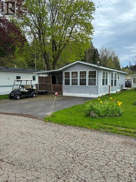 Single-story residence featuring light gray siding, multiple large windows, and a covered porch with a wood-slat privacy screen - 580 Beaver Creek Road Unit# 203, Waterloo, ON - Outdoor