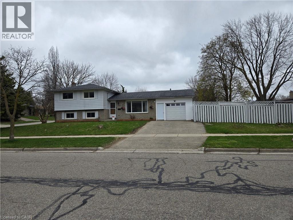 Split-level residence featuring a brick and siding exterior, an attached single-car garage, a concrete driveway, a manicured lawn, and a white picket fence - 261 Overlea Drive, Kitchener, ON