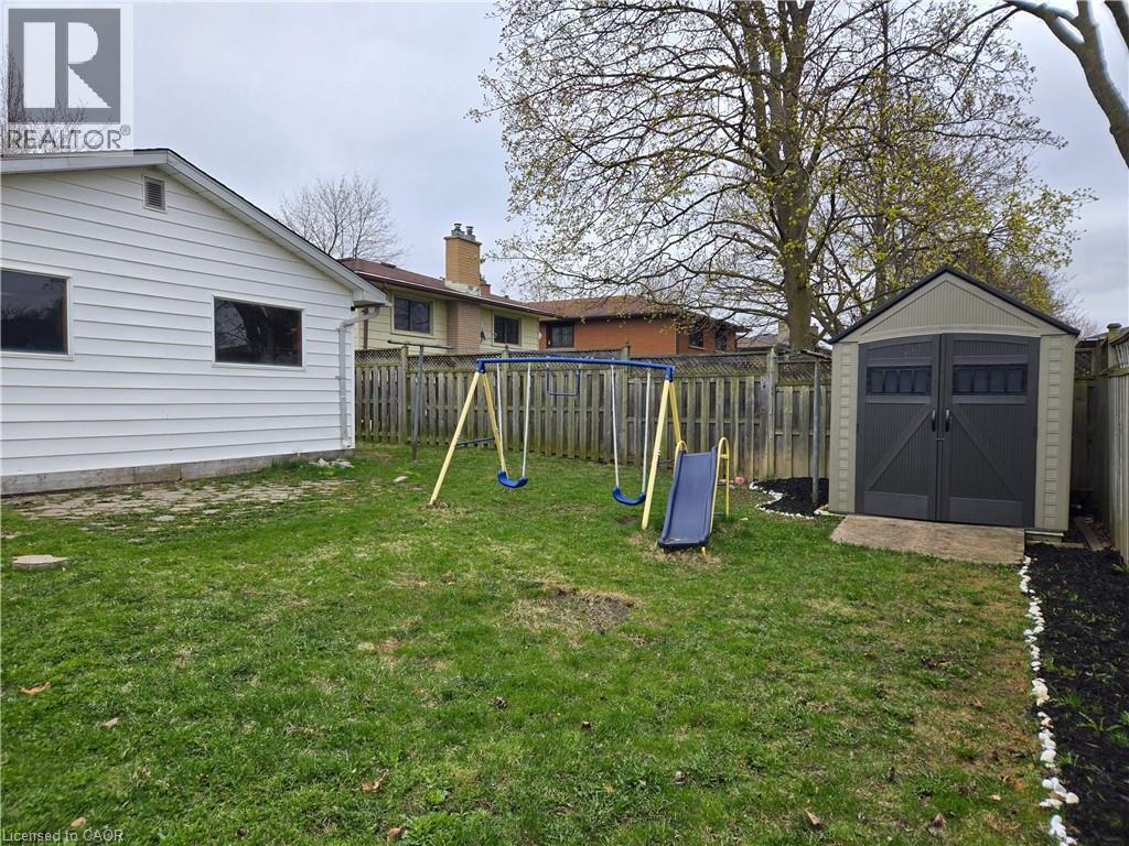 Expansive backyard featuring a manicured lawn, a privacy fence, and a dedicated storage shed on a concrete pad - 261 Overlea Drive, Kitchener, ON