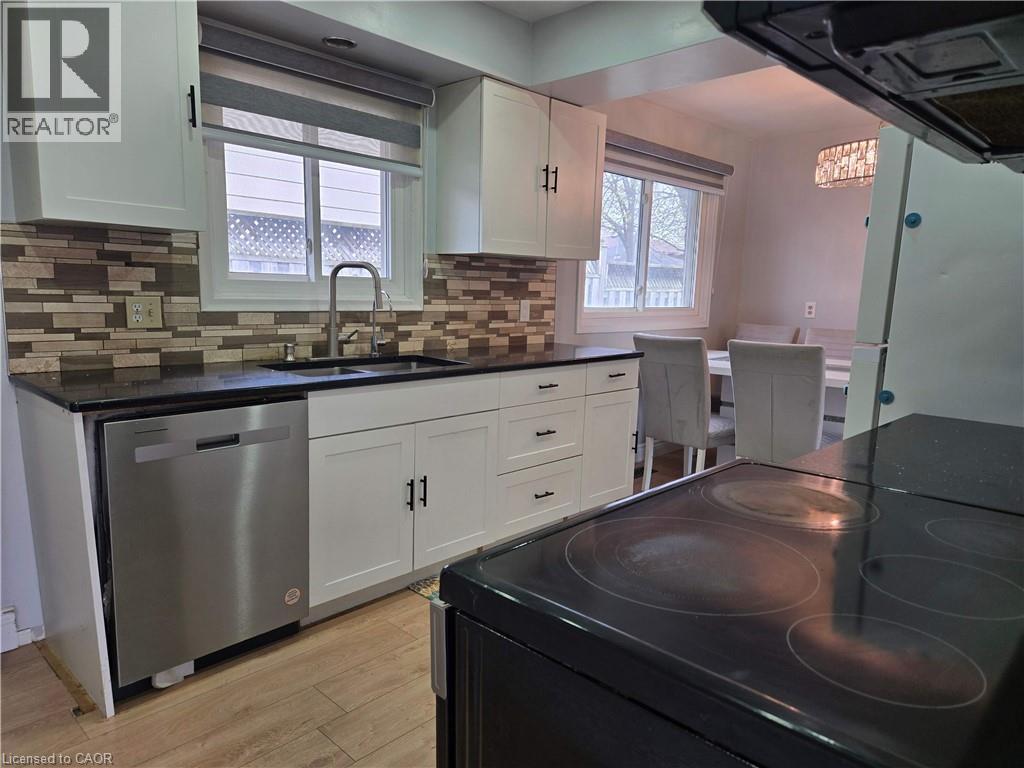 Kitchen featuring white cabinetry, dark countertops, a mosaic tile backsplash, a stainless steel dishwasher, and wood-finish flooring - 261 Overlea Drive, Kitchener, ON