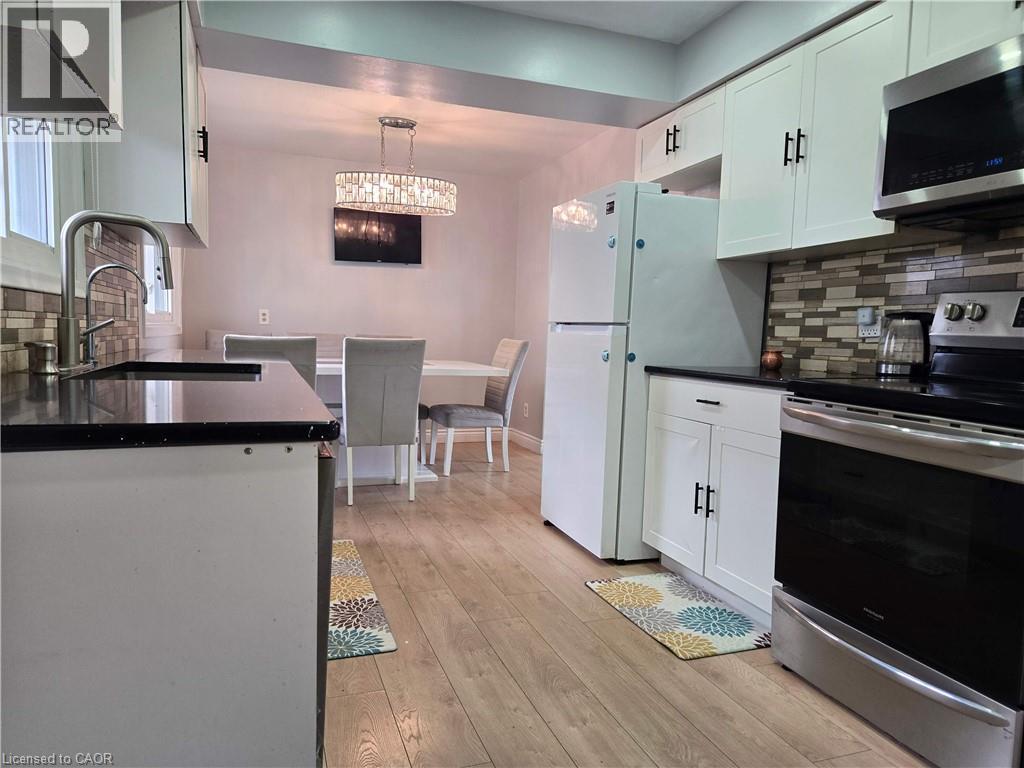 Kitchen featuring light wood-finish flooring, white cabinetry with black hardware, dark countertops, and a mosaic tile backsplash - 261 Overlea Drive, Kitchener, ON