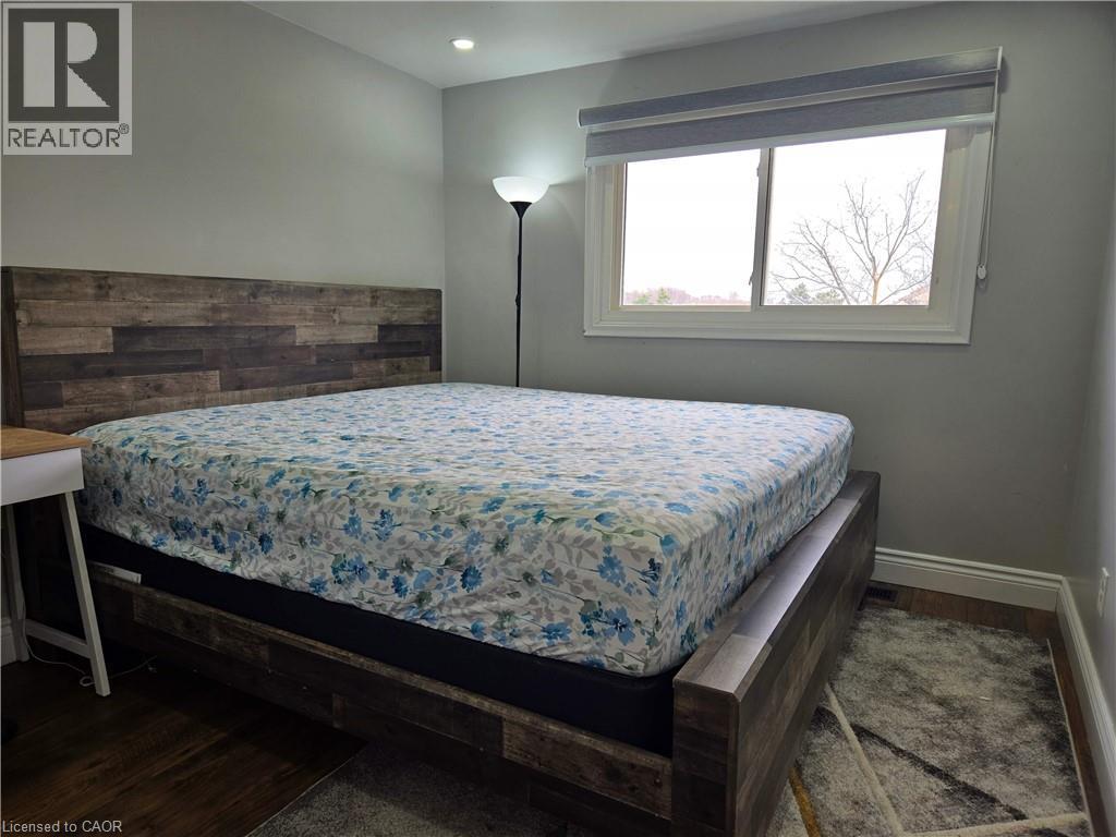 Room featuring light gray painted walls, a white-framed window with a roller shade, and dark wood-finish flooring - 261 Overlea Drive, Kitchener, ON