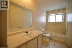 Bathroom featuring a large vanity with an integrated sink, an expansive wall-mounted mirror, a tiled tub-shower combination, a white toilet, and a window with privacy glass -