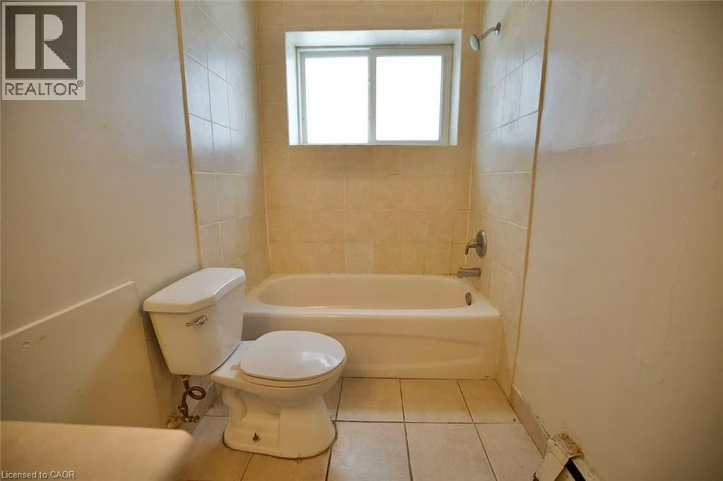 Bathroom featuring a white bathtub, ceramic wall tiling, shower fixture, and a white toilet - 223 Heiman Street, Kitchener, ON - Indoor Photo Showing Bathroom