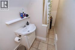 Compact bathroom featuring a white sink with a vanity cabinet, a wall-mounted shelf, and tiled flooring -