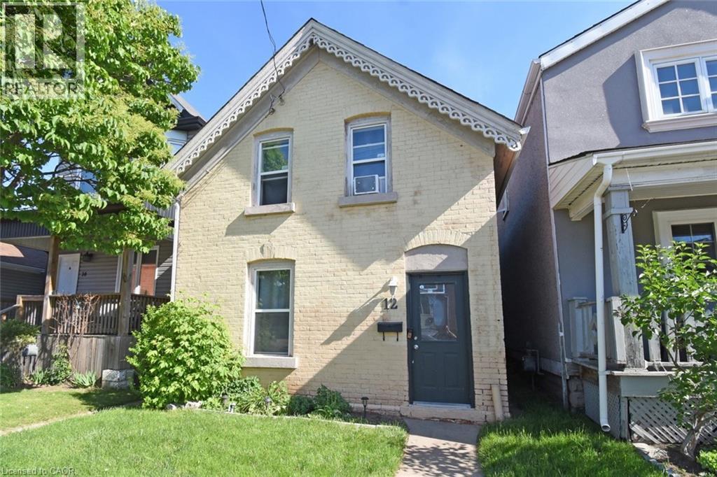 Brick exterior with decorative gable trim, a dark-colored entry door, and a manicured lawn - 12 Wood Street W, Hamilton, ON - Outdoor