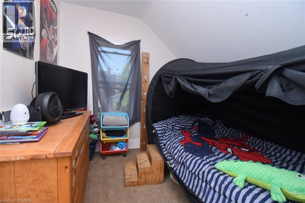 Attic room featuring an angled ceiling, a single window with dark mesh covering, light-colored walls, and carpet flooring - 12 Wood Street W, Hamilton, ON - Indoor