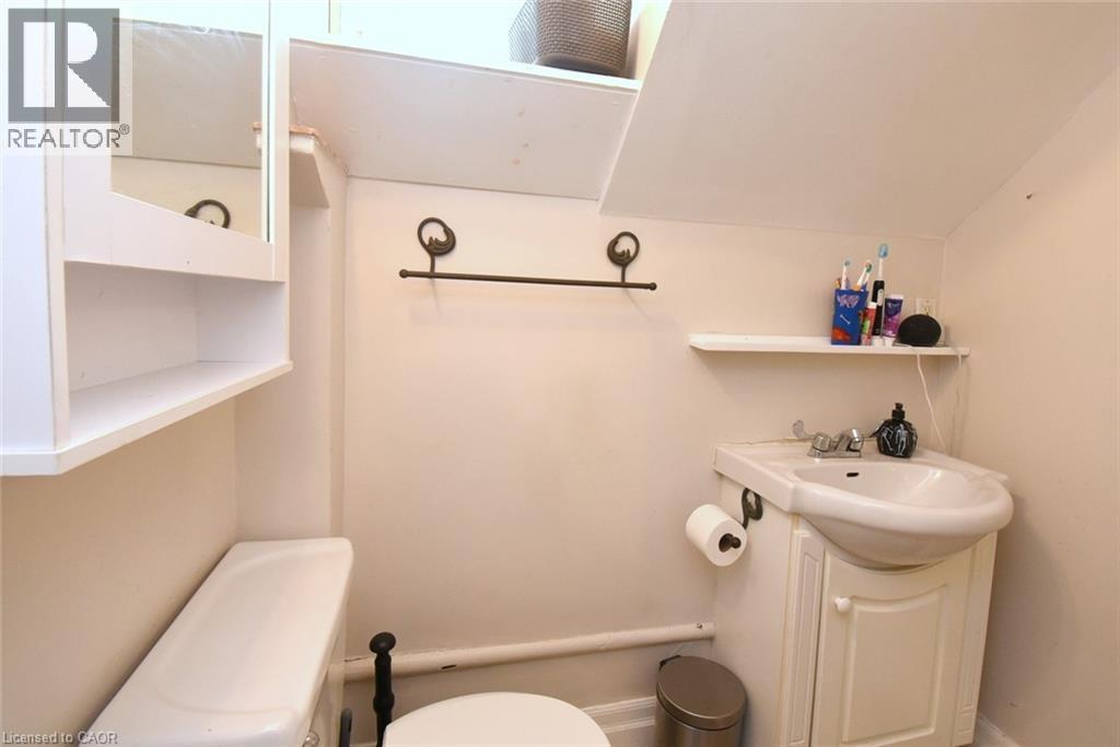 Compact bathroom featuring a white porcelain toilet, pedestal sink with integrated vanity, mirrored medicine cabinet with open shelving, and wall-mounted towel bar - 12 Wood Street W, Hamilton, ON - Indoor Photo Showing Bathroom