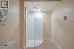 Corner shower with frosted glass enclosure, white tile base, and chrome fixtures -