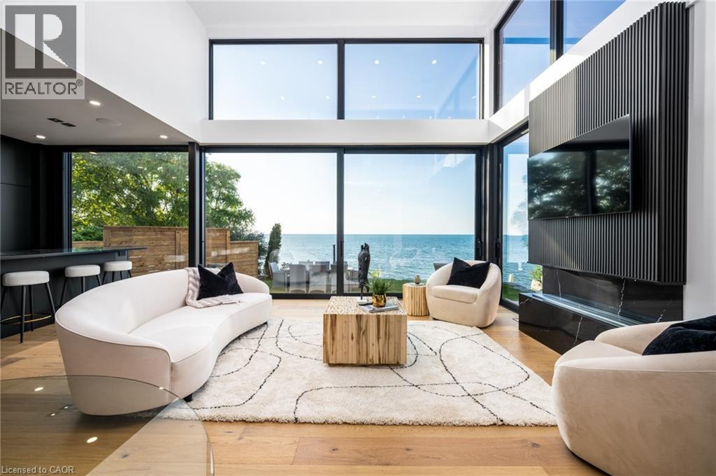 Spacious living area featuring expansive floor-to-ceiling windows, high ceilings, wood-finish flooring, a contemporary fireplace with a dark stone surround, and a built-in bar area - 6 Firelane 11A Street, Niagara-On-The-Lake, ON - Indoor Photo Showing Living Room