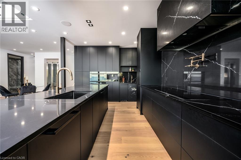 Modern kitchen featuring black flat-panel cabinetry, a black island with an undermount sink and gold-tone faucet, light wood-finish flooring, and black countertops with a distinctive white veining pat - 6 Firelane 11A Street, Niagara-On-The-Lake, ON - Indoor Photo Showing Kitchen With Upgraded Kitchen