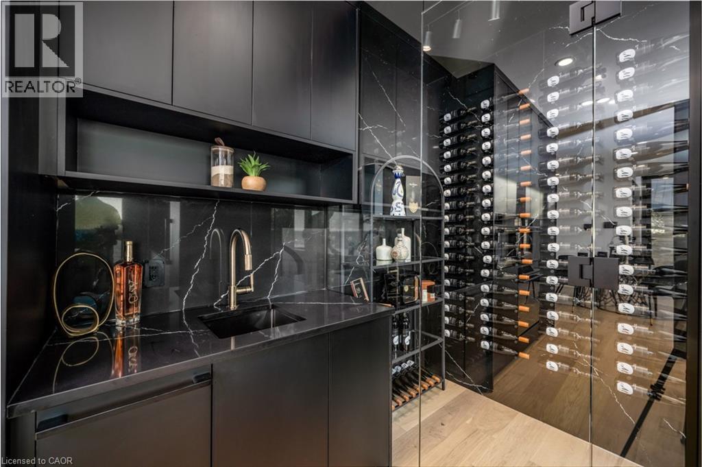 Integrated wet bar featuring a black undermount sink with a gold-tone faucet, black cabinetry, and a stone-finish countertop and backsplash - 6 Firelane 11A Street, Niagara-On-The-Lake, ON - Indoor Photo Showing Other Room