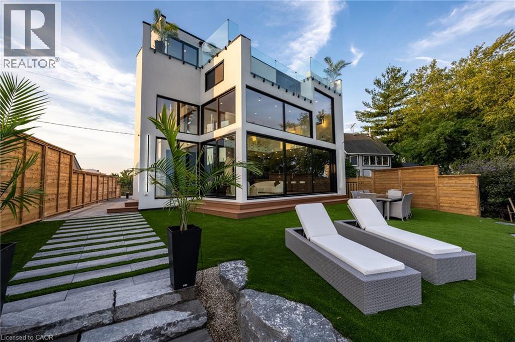 Modern multi-story residence featuring expansive glass panels, a rooftop terrace with glass railings, and a wood-decked patio - 6 Firelane 11A Street, Niagara-On-The-Lake, ON - Outdoor With Deck Patio Veranda