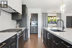 Contemporary kitchen featuring dark cabinetry, light countertops, wood-finish flooring, a kitchen island with an integrated sink and black faucet, and a large window with exterior greenery -