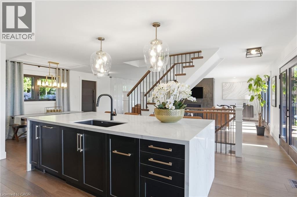 Spacious kitchen island featuring a white countertop, undermount sink, matte black faucet, and dark cabinetry with brass-tone hardware - 71 Miles Road, Hamilton, ON