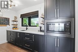 Built-in microwave oven surrounded by dark cabinetry with polished hardware, white countertops, and a black sink with a matching faucet -
