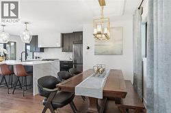 Open-concept kitchen and dining area featuring dark cabinetry, white countertops, a built-in range hood with matching backsplash, and wood-finish flooring -