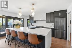 Modern kitchen featuring a large waterfall island with integrated sink, black cabinetry, stainless steel appliances, and wood-finish flooring -
