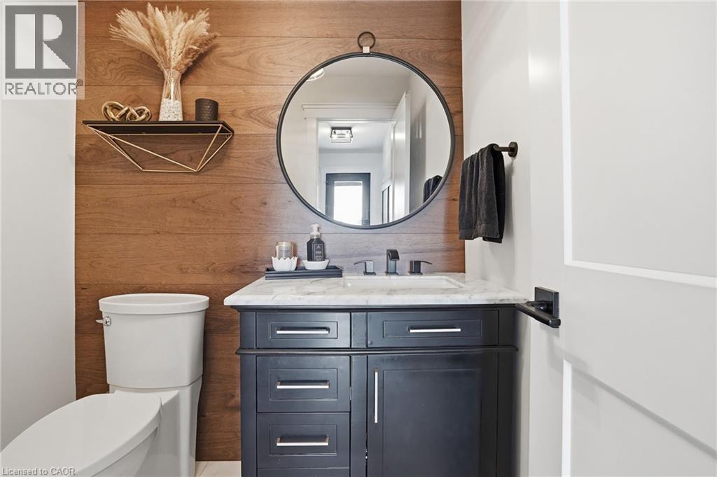 Powder room featuring a wood-panel accent wall, dark wood-finish vanity with a white countertop, and a circular wall-mounted mirror - 71 Miles Road, Hamilton, ON