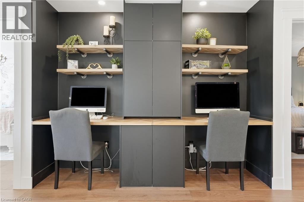 Dedicated dual workspace featuring built-in cabinetry, floating wood shelves with industrial-style brackets, a continuous wood-finish countertop, and recessed lighting - 71 Miles Road, Hamilton, ON
