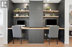 Dedicated dual workspace featuring built-in cabinetry, floating wood shelves with industrial-style brackets, a continuous wood-finish countertop, and recessed lighting -