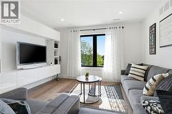 Light-filled living area featuring wood-finish flooring, a contemporary built-in media console with glossy white cabinetry, and a prominent window with dark framing -