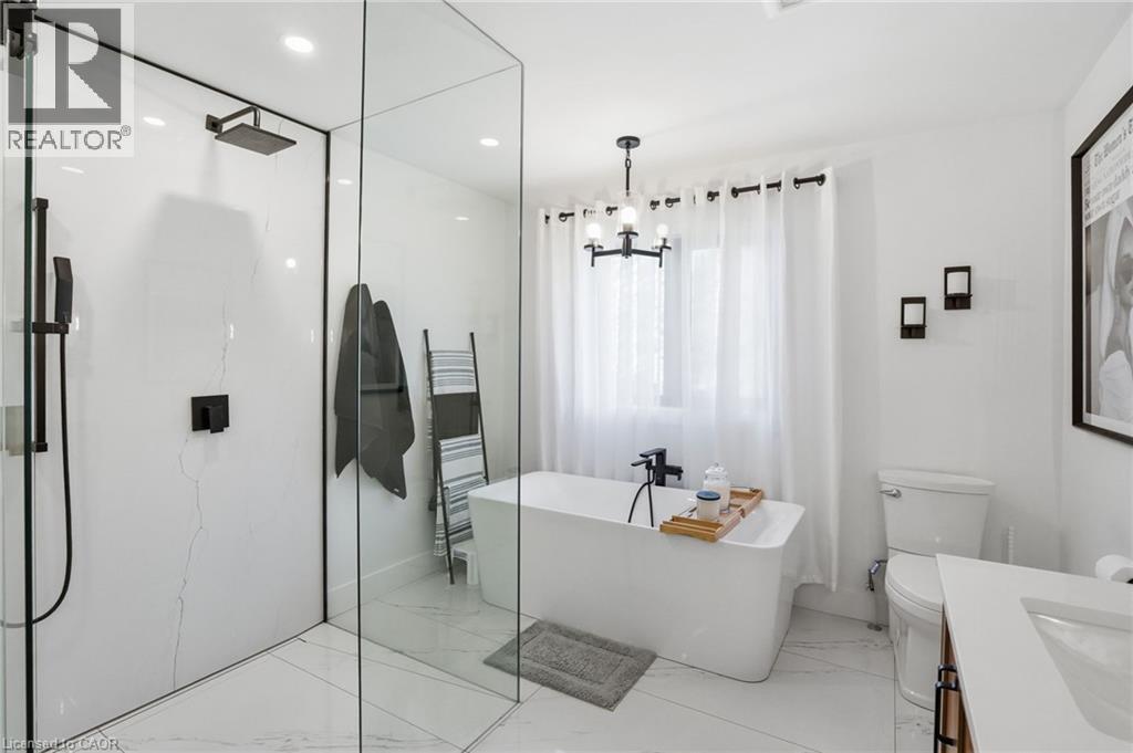 Contemporary bathroom featuring a frameless glass shower enclosure, a standalone soaking tub with matte black fixtures, and a modern chandelier - 71 Miles Road, Hamilton, ON