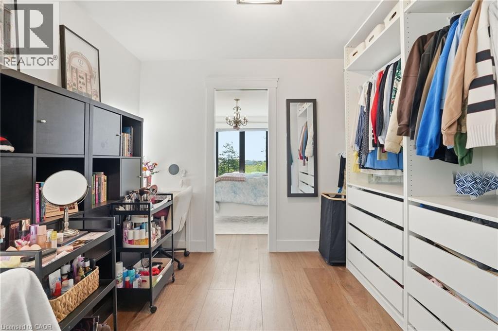 Walk-in closet featuring light wood-finish flooring, white walls, and built-in closet systems with shelving and drawers - 71 Miles Road, Hamilton, ON