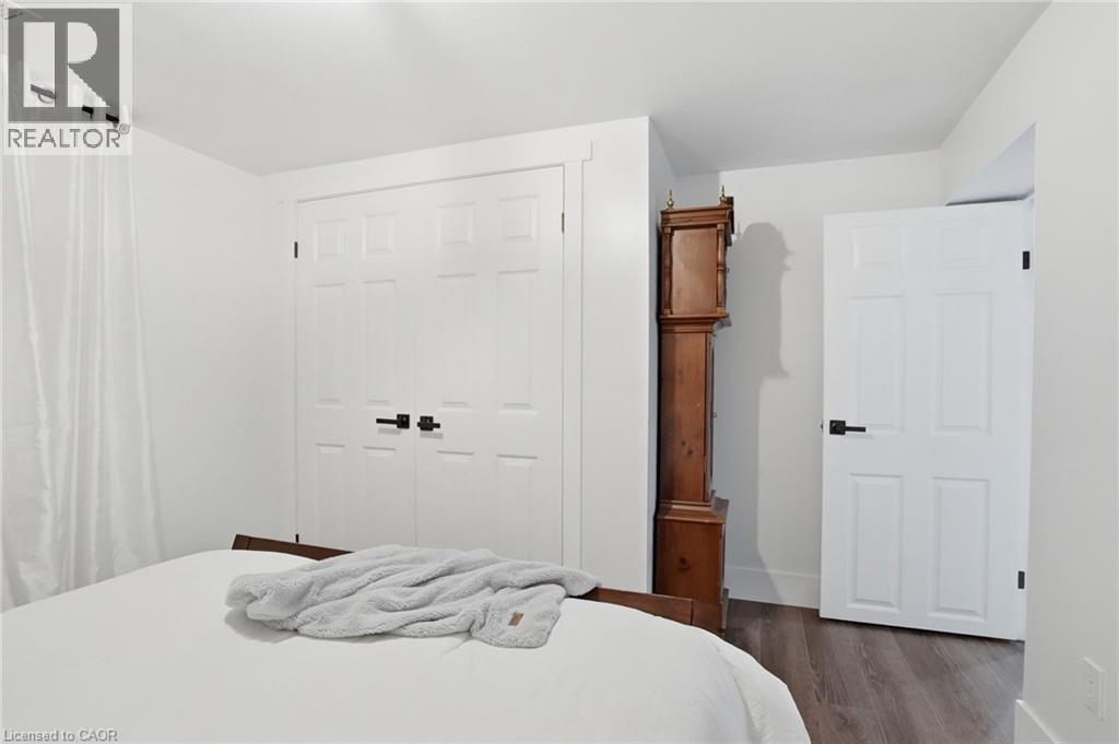 Interior space featuring wood-finish flooring, white paneled doors with black hardware, and ample natural light from a window with sheer white curtains - 71 Miles Road, Hamilton, ON