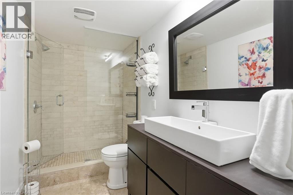 Modern bathroom featuring a frameless glass shower enclosure, beige tile shower surround, and a rectangular vessel sink - 71 Miles Road, Hamilton, ON