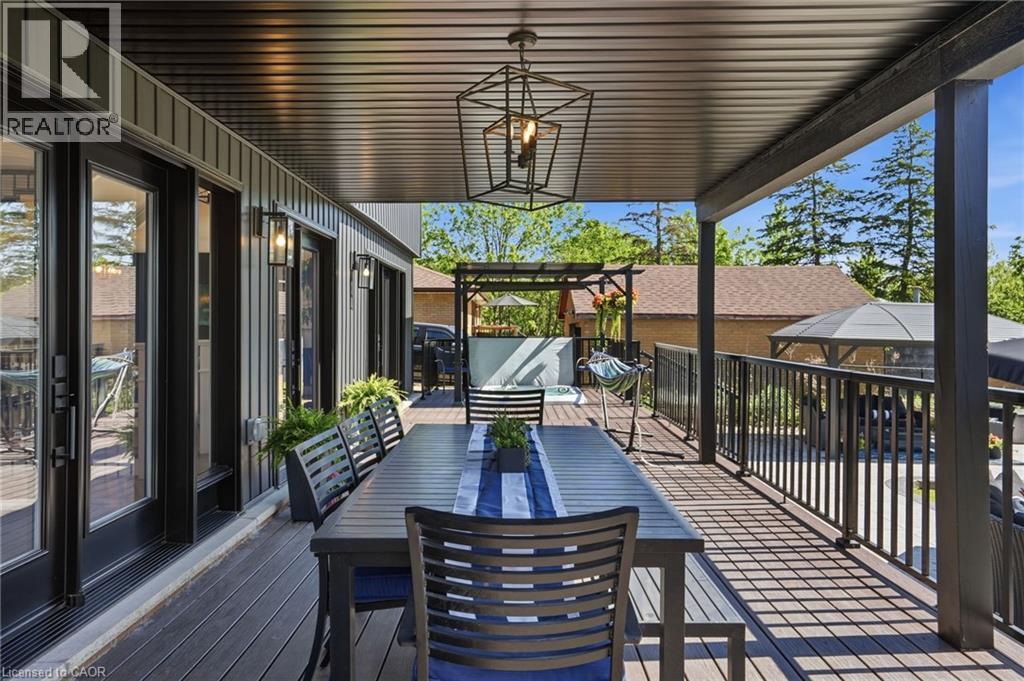 Expansive covered deck featuring composite decking, black metal railings, and a contemporary geometric pendant light - 71 Miles Road, Hamilton, ON
