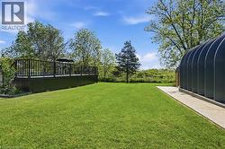 Spacious outdoor area featuring a broad green lawn, a raised wooden deck with dark railings, and a large arched metal structure -
