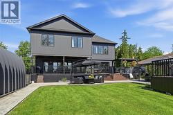 Spacious rear yard with a manicured lawn, dark composite decking, multiple outdoor living areas, and a detached storage structure -