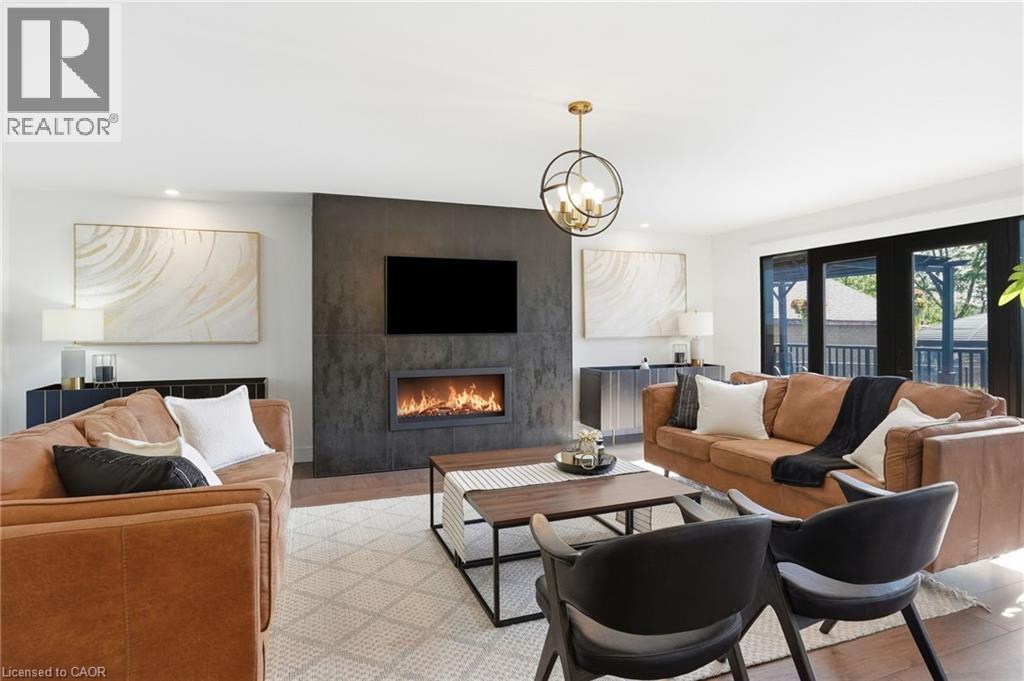 Spacious living area featuring a modern fireplace insert within a dark textured accent wall, recessed lighting, a contemporary brass chandelier, and dark-framed double doors opening to an exterior are - 71 Miles Road, Hamilton, ON